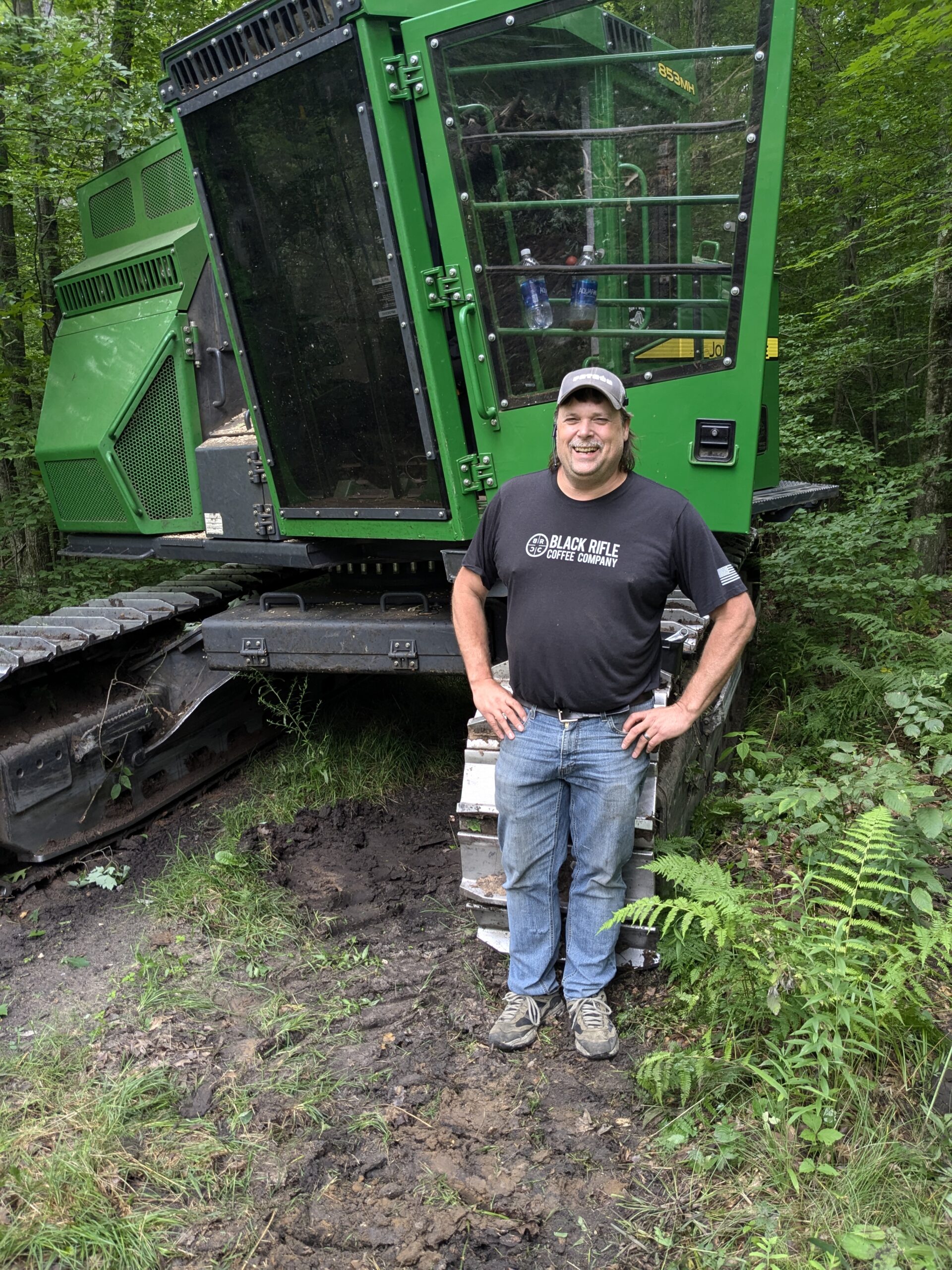 Charlie Harris, owner of Northern MI Forestry, standing next to John Deere Harvester in Michigan forest