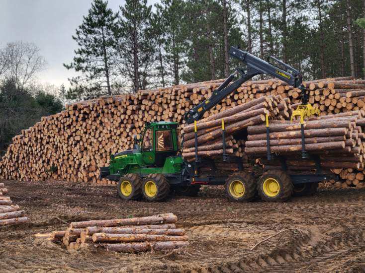 harvester loading logs in stacks at staging site of forestry project in Michigan